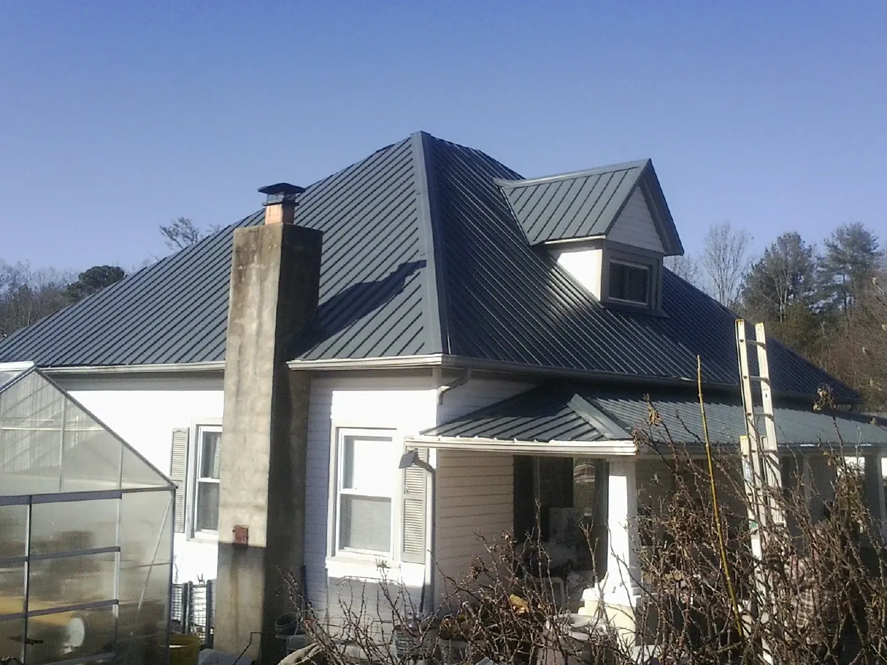 Dark blue standing seam metal roof on a white farmhouse with dormer — Slate & Tile Roof Repair by Roofing Brothers in Lake Jackson
