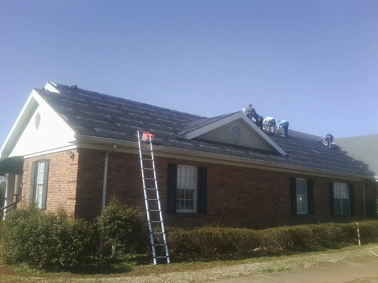 Crew tearing shingles off a brick ranch roof with a ladder set — Emergency Roof Repair work by our crew in Lake Jackson