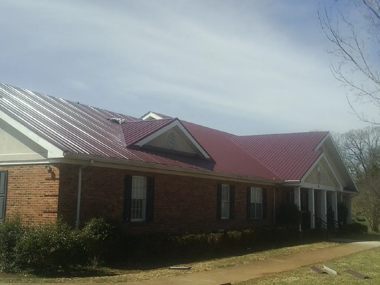 Red metal roof with gabled entries on a long brick building, from a Hail Damage Roof Repair job in Lake Jackson