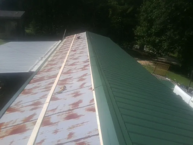 Old rusted panels beside newly installed green metal roofing — Wind Damage Roof Repair by Roofing Brothers in Lake Jackson