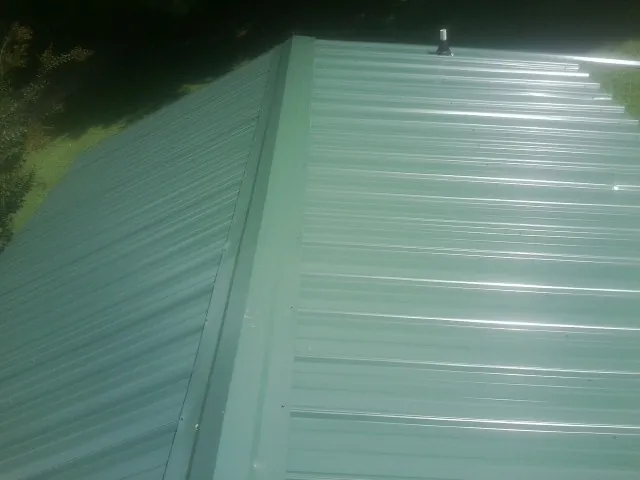 New green metal panels meeting at the ridge of a roof — Flat Roof Repair work by our crew in Lake Jackson