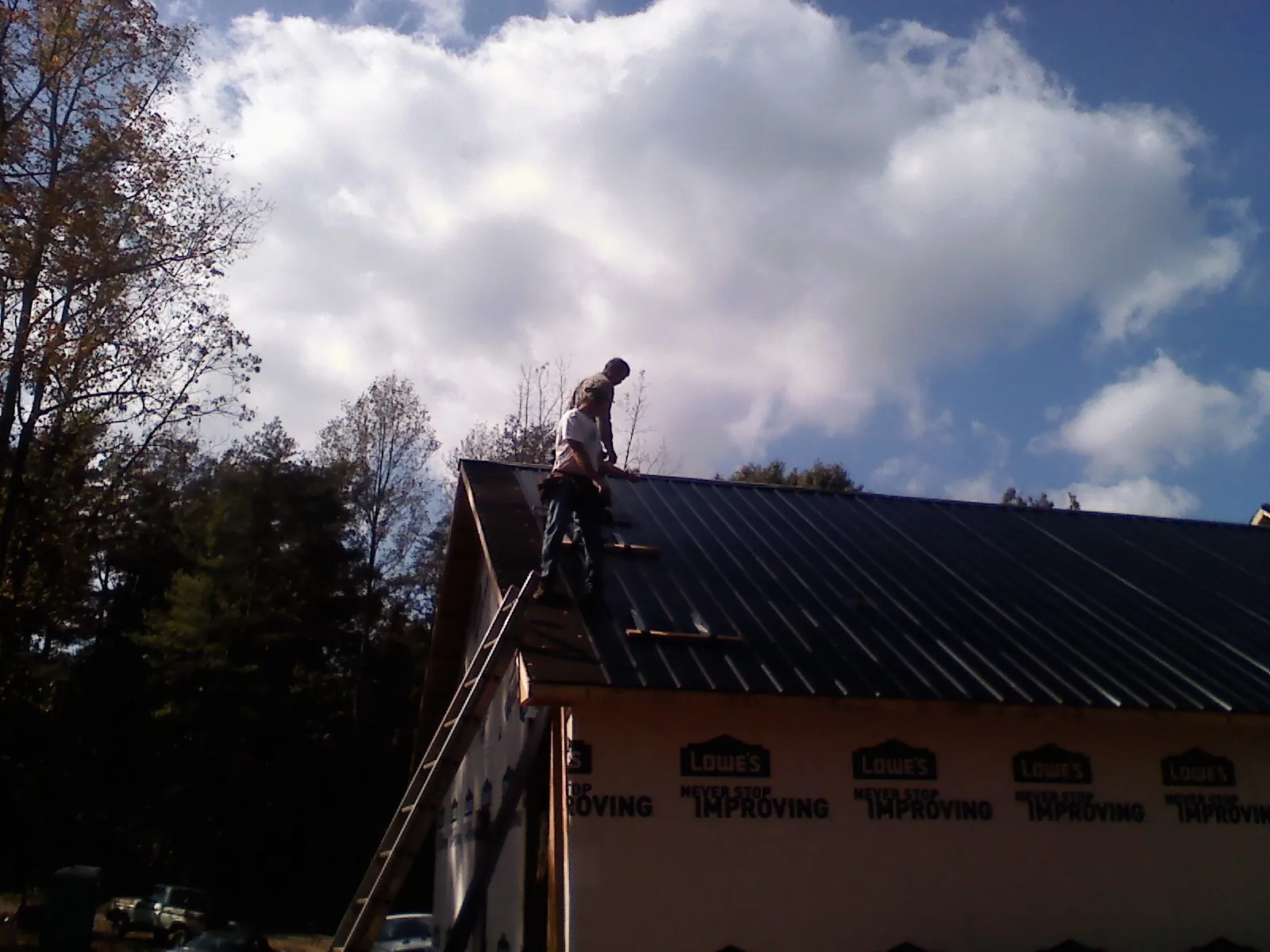 Roofer fastening dark metal panels high against a cloudy sky, from a Roof Inspection job in Lake Jackson